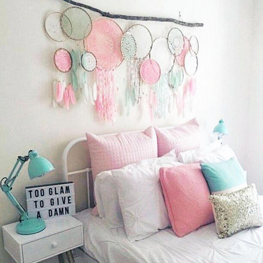 Chambre avec un lit blanc, une branche avec plusieurs commodes de rêve suspendues et des oreillers roses et bleus.  Sur le mur blanc 