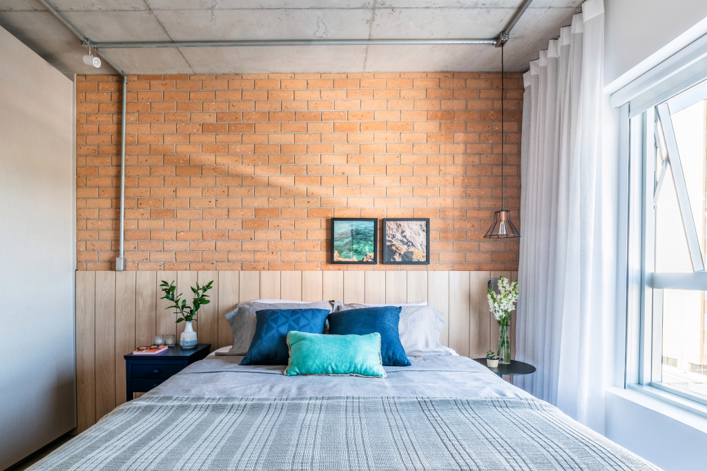 Chambre double de style industriel, avec tête de lit à lattes de bois, avec mur de briques semi-orange.