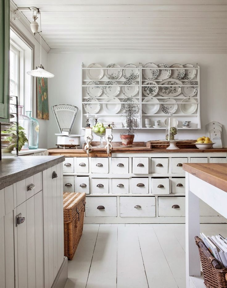 Cuisine avec comptoirs en bois blanc en dessous et dessus en bois foncé.  Plats avec des fleurs sur des étagères sur le mur.  Échelle rustique, pommes et poires sur le comptoir.