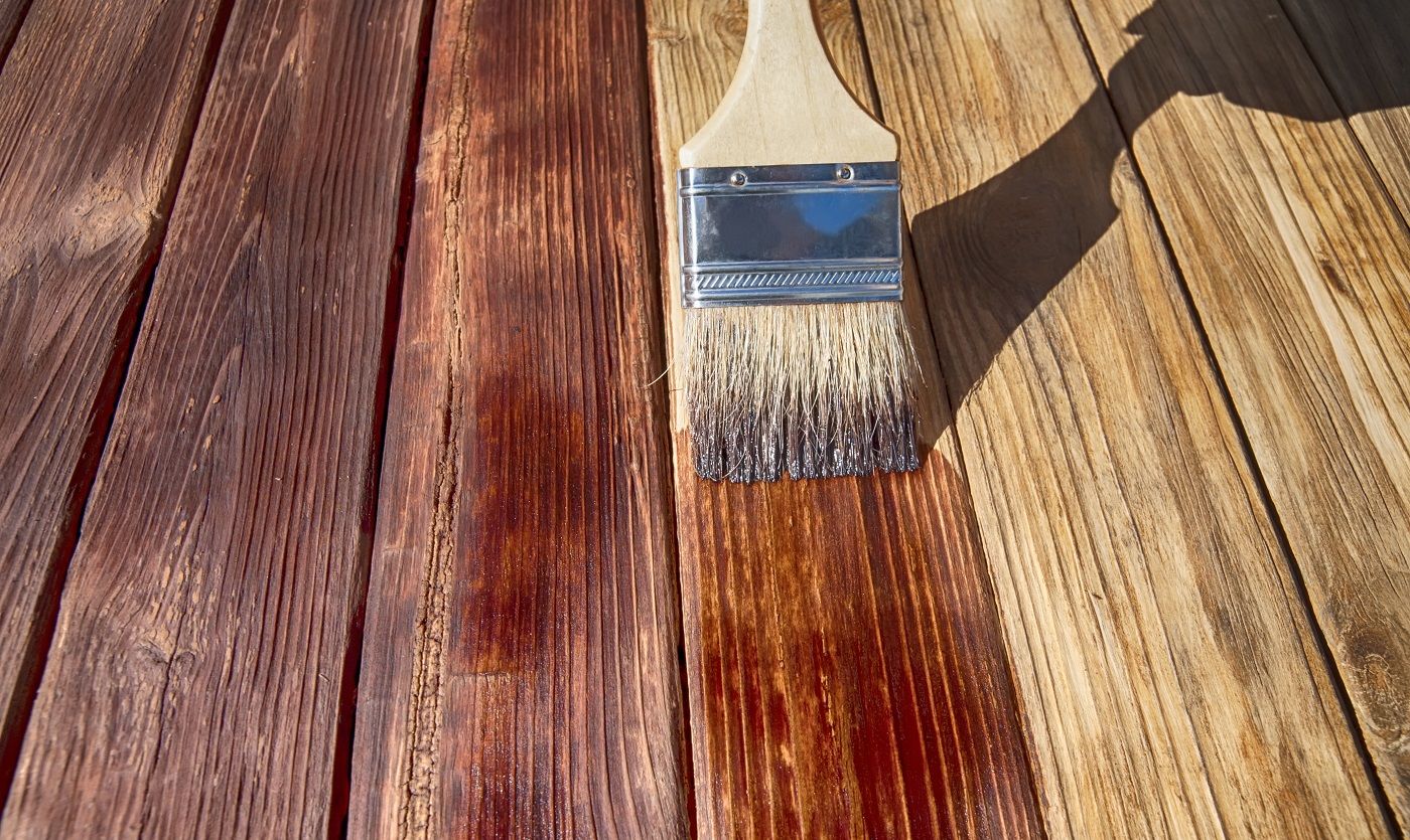 Une brosse en bois recouvre la surface de la planche de bois avec une tache rouge foncé vue de côté avant close up