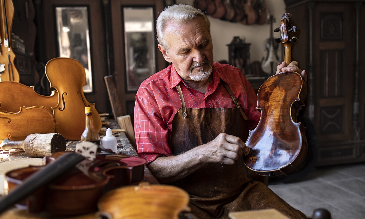 Artisan menuisier senior polissant l'instrument de violon dans son atelier de menuiserie.