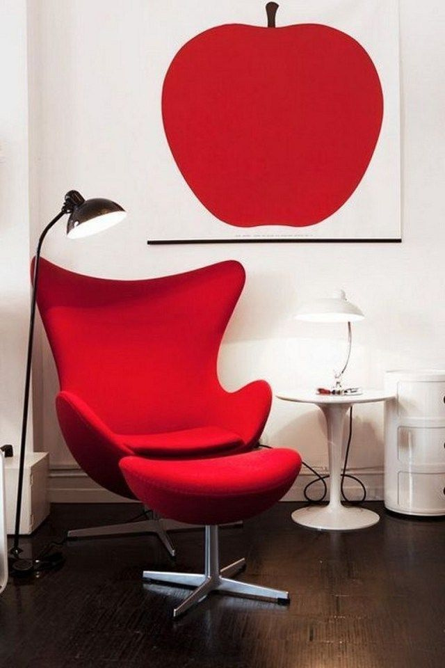 Chaise œuf rouge vif.  Table d'appoint avec lampe, toutes deux blanches.  Parquet, lampadaire métallique à gauche.  Sur le mur blanc, une photo avec une pomme dans la même teinte de rouge que la chaise.