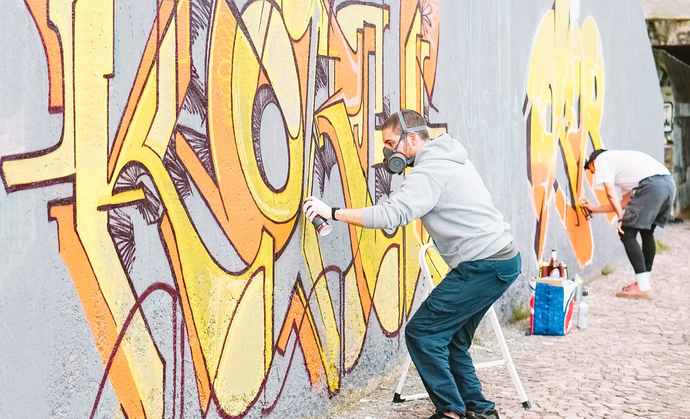 Artistes de graffiti peignant une peinture murale colorée sur un mur gris - Hommes créatifs exécutant des peintures murales de dessin - Concept d'art de rue et moderne, de culture et de mode de vie des jeunes