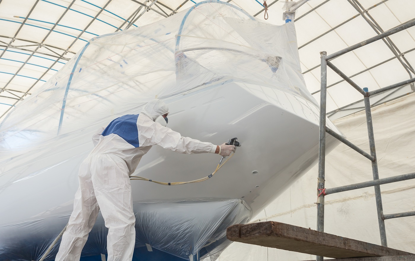 Travailleur portant un uniforme de protection et pulvérisant de la peinture sur le bateau