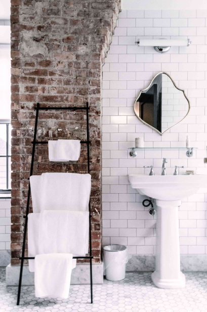Ici, l'élément cohabite avec la maçonnerie d'origine exposée dans une zone de la salle de bain.  Le cadre intemporel est complété par un sol carrelé, un lavabo sur pied et un éclairage vintage.
