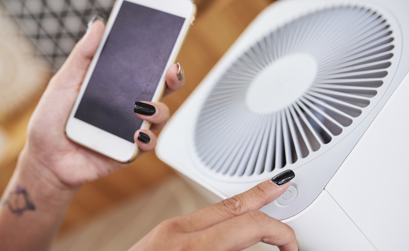 Image en gros plan d'une femme allumant le climatiseur et utilisant l'application Smart Home sur son téléphone pour gérer la température