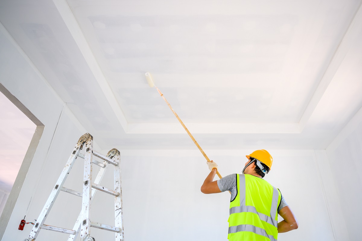 Jeune travailleur de la construction de sexe masculin asiatique Travailler comme peintre en bâtiment Peindre le plafond à l'intérieur de la maison et utiliser un rouleau de peinture d'apprêt blanc sur le chantier de construction.  Comment peindre un plafond en le résumant.