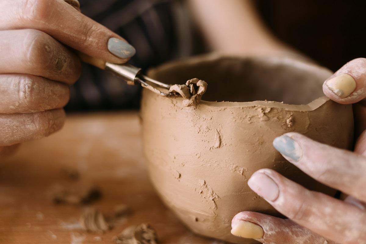 les mains d'un potier d'argile sculptent un motif sur le bol.  Vue de côté.  Céramique et argile pour la créativité en atelier.  outil de sculpture, gros plan.  Choses à retenir lors de l'achat d'outils de sculpture en argile.