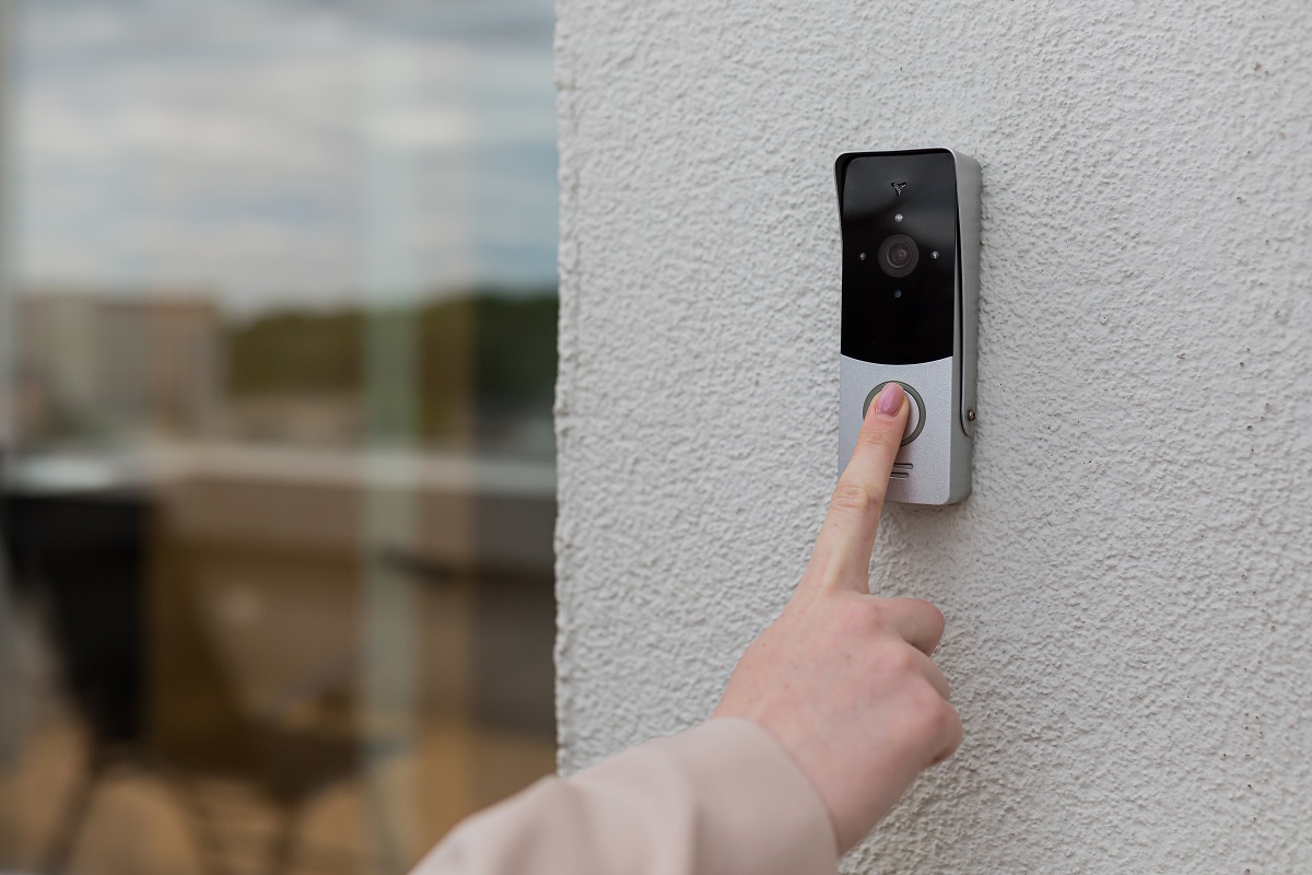 la main de la femme utilise une sonnette sur le mur de la maison avec une caméra de surveillance.  Qu'est-ce qu'une sonnette sans fil.
